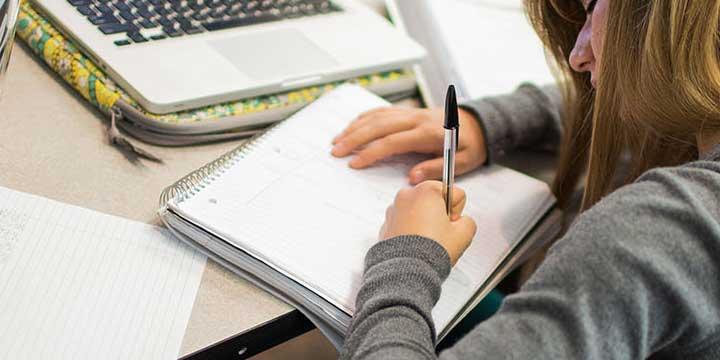 年轻女子在笔记本电脑前的桌子上用螺旋笔记本写字